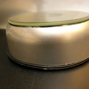 May include: A silver rotating display stand with a clear glass top. The stand is ideal for showcasing small items such as jewellery, figurines, or collectibles.