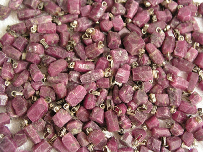 May include: A large group of small, rough, pink ruby gemstone pendants with silver jump rings.