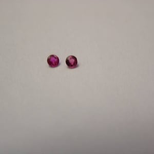 May include: Two small, oval-shaped, pink gemstones on a white background.