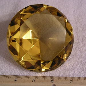 May include: A large, faceted, golden yellow crystal paperweight. The crystal is shaped like a diamond and has a high polish.