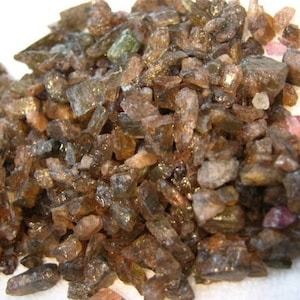 May include: A pile of small, brown, and pink gemstones. The gemstones are rough and have a variety of shapes and sizes.