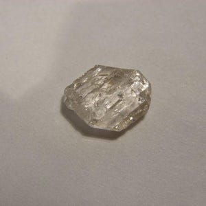 May include: A clear, faceted, hexagonal diamond crystal.
