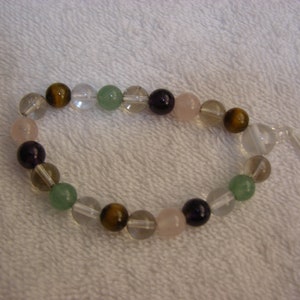 Könnte beinhalten: Ein Armband aus verschiedenen Edelsteinperlen, darunter klarer Quarz, Tigerauge, Amethyst, Rosenquarz und grüner Aventurin.