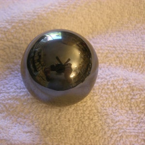 May include: A smooth, black, spherical object with a reflective surface. The object is sitting on a white, textured surface.