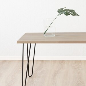 May include: A light wood table with black hairpin legs. A single green leaf is in a clear glass vase on the table.