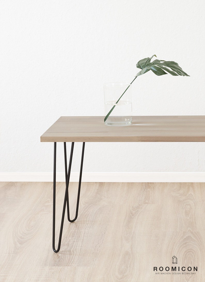 May include: A light wood table with black hairpin legs. A single green leaf is in a clear glass vase on the table.