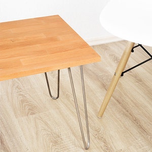 May include: A light wood coffee table with a rectangular top and hairpin legs. The table is sitting on a light wood floor.
