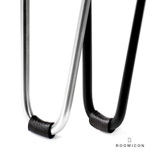 May include: Close-up of two metal hairpin legs with black leather padding on the bottom. The legs are in a U-shape and are made of silver and black metal.