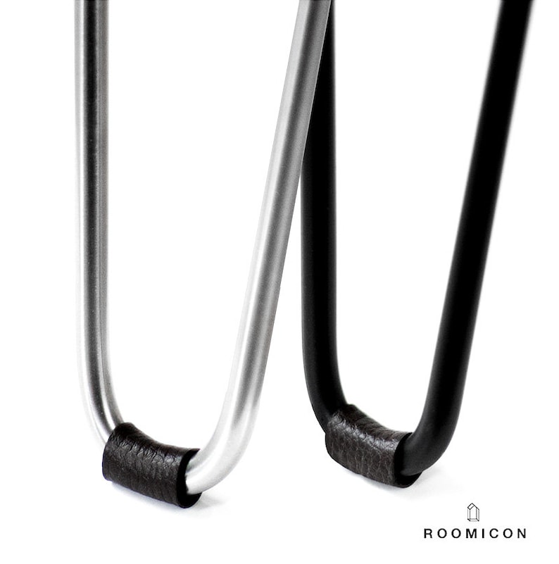 May include: Close-up of two metal hairpin legs with black leather padding on the bottom. The legs are in a U-shape and are made of silver and black metal.