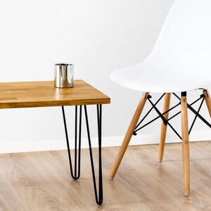 May include: A wooden coffee table with black hairpin legs and a silver metal container on top. The table is next to a white chair with wooden legs.