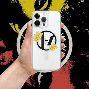 Puede incluir: Funda transparente para teléfono con un logotipo negro y amarillo con las letras "-Z-" y dos flores de margarita amarillas. La funda del teléfono se sostiene en una mano sobre un fondo colorido.
