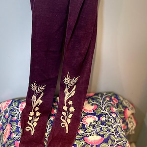 May include: Deep purple tights with gold floral embroidery near the ankles. The tights are made of a soft, velvety material. The background features a blue floral patterned fabric.
