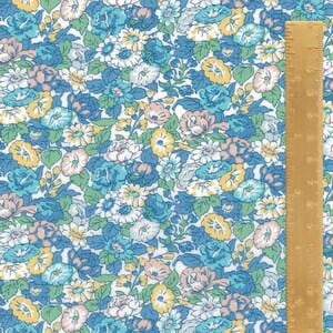 May include: Floral fabric with a pattern of blue, white, and yellow flowers on a white background. A wooden ruler is placed on the right side of the fabric, showing measurements in inches.