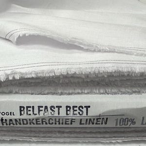 May include: A stack of white fabric with frayed edges and a black stitched line near the border. The packaging is labeled with black text reading Spechler-Vogel Textiles, Belfast Best, Handkerchief Linen, and 100% Linen in a clear font.
