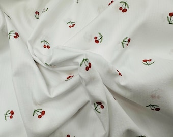 May include: White fabric with a repeating pattern of red cherries with green stems. The fabric is folded and wrinkled.