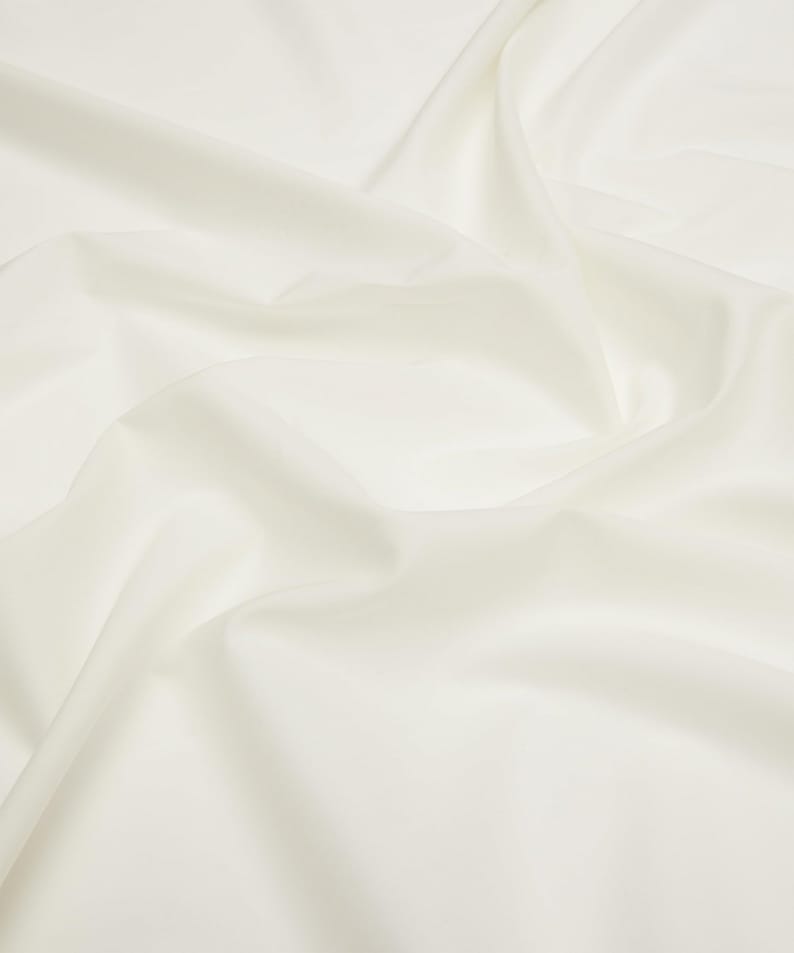 May include: A smooth, white fabric with soft folds and wrinkles. The fabric is a light, creamy white color and has a subtle sheen.