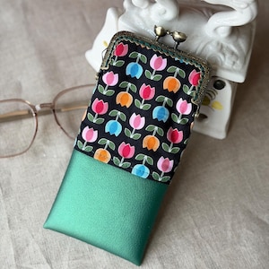 Könnte beinhalten: Eine rechteckige Tasche mit einem Metall-Schnappverschluss. Der obere Teil besteht aus schwarzem Stoff mit einem wiederkehrenden Muster aus bunten Tulpen in Pink, Blau und Orange. Der untere Teil besteht aus einem einfarbigen, metallisch grünen Material.