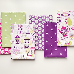 May include: Several folded fabric pieces with diverse patterns. Designs include white polka dots on green and purple, floral patterns in pink and purple, a neighbourhood scene, and a tea party theme with teacups and cakes.