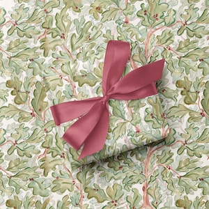 May include: A rectangular gift box wrapped in paper featuring a repeating pattern of green oak leaves and small red acorns on a cream background, tied with a wide, smooth, dark pink satin ribbon arranged in a decorative bow.
