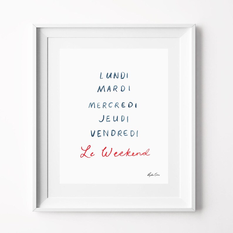 May include: A white framed wall art print featuring the French days of the week in dark blue handwritten text: Lundi, Mardi, Mercredi, Jeudi, Vendredi, followed by the phrase Le Weekend in red handwritten script, with a small signature at the bottom.