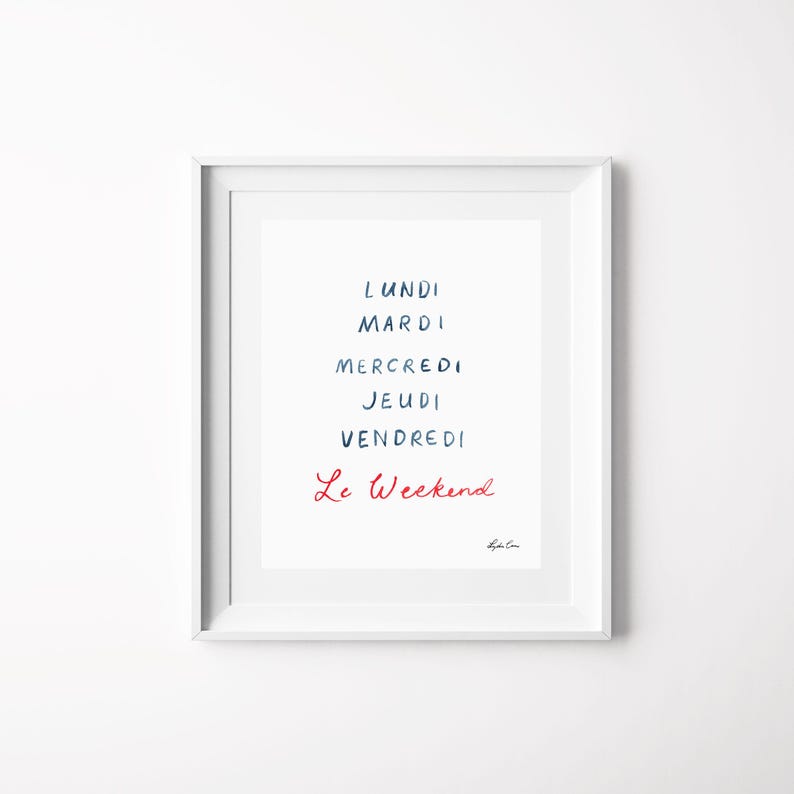 May include: A white framed wall art print featuring the French days of the week in dark blue text: Lundi, Mardi, Mercredi, Jeudi, Vendredi, followed by the phrase Le Weekend in red cursive script. A small signature is visible in the bottom right corner.