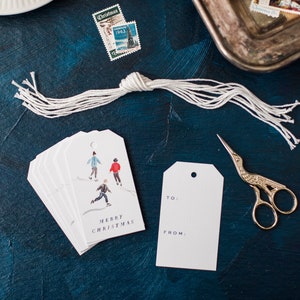 May include: A set of white gift tags with a watercolor illustration of people ice skating. The tags say "Merry Christmas" and have a space for "To" and "From".