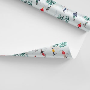 May include: A roll of white wrapping paper with a repeating pattern of skiers in colorful clothing on a snowy mountain landscape. The paper is partially unrolled, revealing the pattern.