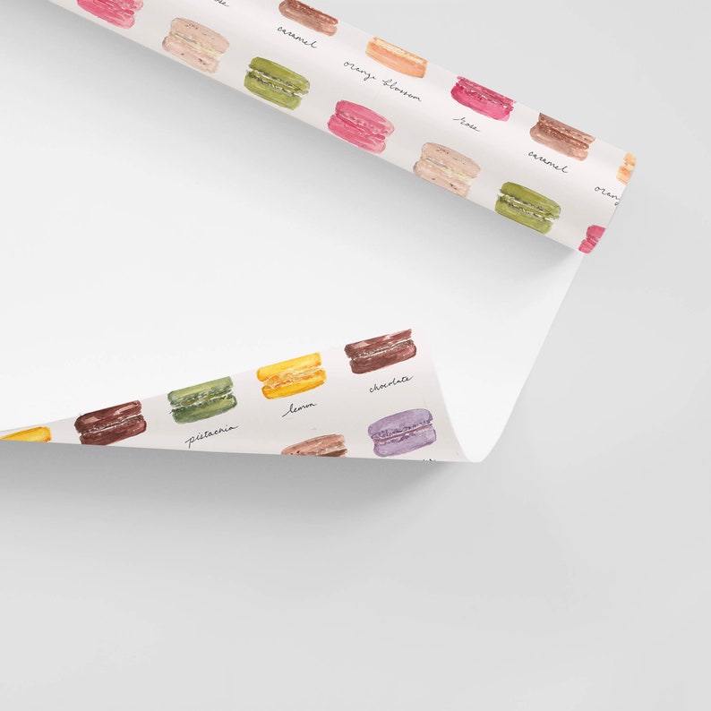 May include: A white background with a repeating pattern of colorful macarons with handwritten text labels for each flavor: pistachio, lemon, chocolate, orange blossom, lime, caramel, orange.