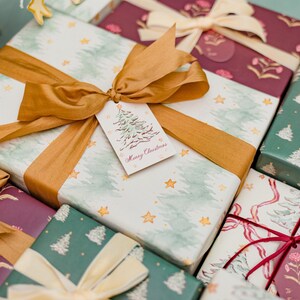 May include: A collection of wrapped Christmas gifts with various patterned papers, including watercolor trees and floral designs. Each gift is tied with a ribbon and bow, some with gift tags that read "Merry Christmas".