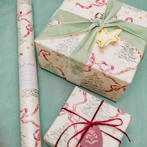 Puede incluir: Papel de regalo y regalos envueltos con tem&aacute;tica navide&ntilde;a. El papel de regalo y los regalos presentan un fondo crema con lazos rojos, &aacute;rboles de Navidad verdes y estrellas doradas. Un regalo est&aacute; atado con una cinta verde y un adorno de estrella dorada.