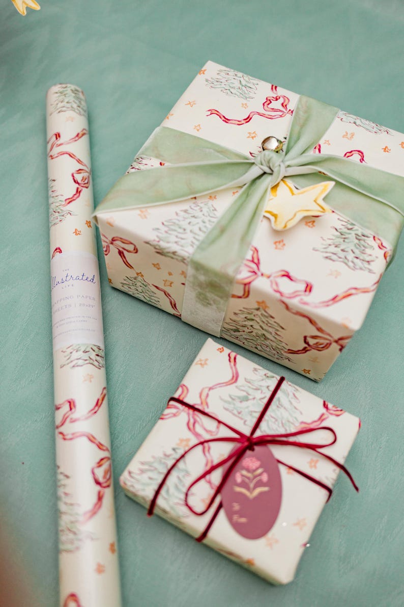 Puede incluir: Papel de regalo y regalos envueltos con tem&aacute;tica navide&ntilde;a. El papel de regalo y los regalos presentan un fondo crema con lazos rojos, &aacute;rboles de Navidad verdes y estrellas doradas. Un regalo est&aacute; atado con una cinta verde y un adorno de estrella dorada.