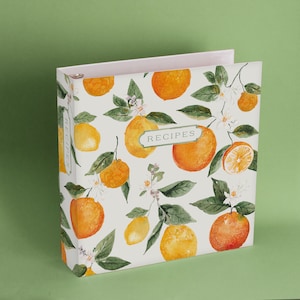 May include: A white recipe binder with a watercolour design of lemons and oranges on a white background. The binder has the word "RECIPES" printed on the front.