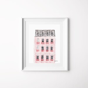 Puede incluir: Una pintura de acuarela de un edificio rosa con un techo gris y balcones rojos. El edificio tiene varias ventanas y est&aacute; pintado en un estilo suave y rom&aacute;ntico.