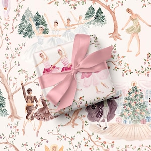 May include: A rectangular gift box wrapped in white paper featuring a watercolor illustration of ballet dancers in pink and white costumes, pine trees, and a decorated Christmas tree, tied with a wide, dusty pink satin ribbon bow.