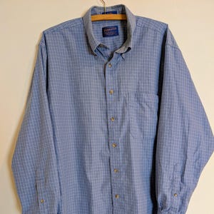 以下が含まれることがあります： 青と白のチェック柄のボタンダウンシャツ、長袖。 シャツはボタンダウンカラー、胸ポケット、茶色のボタンが付いています。 ブランド名「Pendleton」がラベルに表示されています。