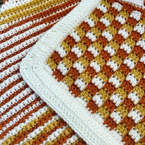 May include: A crocheted blanket with a white border and stripes of orange, yellow, and white.