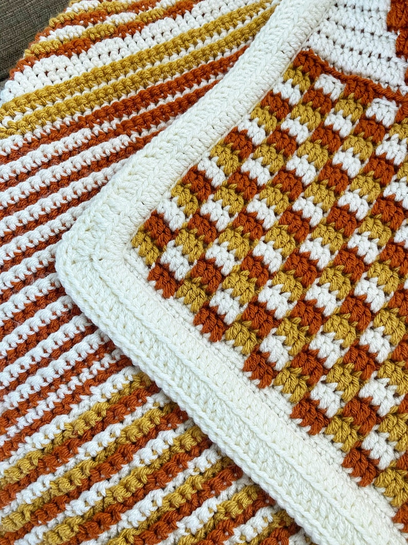 May include: A crocheted blanket with a white border and stripes of orange, yellow, and white.