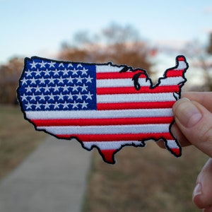 May include: A red, white, and blue embroidered patch shaped like the United States of America. The patch is made of fabric and has a stitched outline.