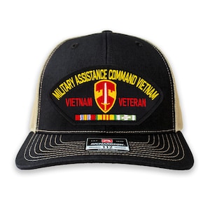 May include: Black and tan trucker hat with a patch that reads "MILITARY ASSISTANCE COMMAND VIETNAM VETERAN". The patch features a yellow and red emblem with a sword and ribbons. The hat is adjustable.