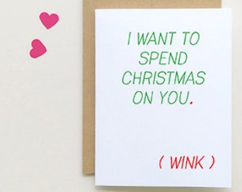 May include: A white card with green text that reads "I want to spend Christmas on you."  The text "(wink)" is written in red below the main text. The card is on a brown background with pink hearts scattered around it.