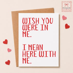 Pode incluir: Cartão de felicitações branco com texto vermelho: «WISH YOU WERE IN ME. I MEAN HERE WITH ME.» O cartão está num envelope castanho, com três decorações em forma de coração vermelhas e rosa.