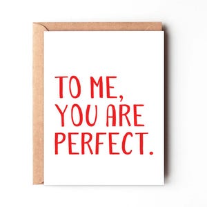 May include: A white greeting card with the text "TO ME, YOU ARE PERFECT" in red. The card is inside a brown envelope. The card is a simple design, perfect for expressing affection.