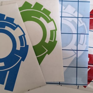 May include: Four vinyl stickers with a stylized gear design. The stickers are blue, green, white, and red.