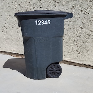 May include: A black wheeled trash can with a white sticker that says "12345".