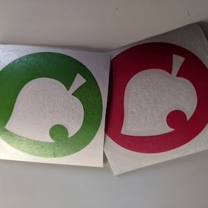 May include: Two white vinyl stickers with a white leaf design. The leaf is inside a circle. One sticker has a green circle and the other has a red circle.