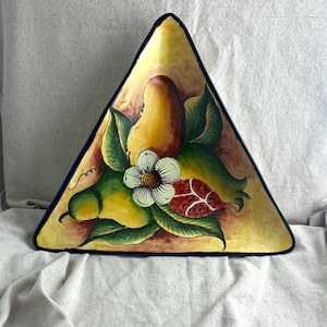 May include: Triangular ceramic serving dish with a hand-painted design. The dish features a yellow background with a central illustration of a yellow fruit, green leaves, a white flower, and a red fruit. The rim is a dark blue.