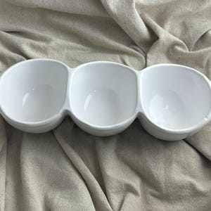 May include: A white ceramic mug with a black handle and the text "But first, coffee" in a handwritten style. The mug is on a white surface. The mug is approximately 4 inches tall.