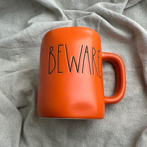 May include: A set of three ceramic mugs with a speckled, matte finish. Each mug features a different color: light blue, cream, and gray. The mugs have a simple, modern design with a rounded shape and a comfortable handle.