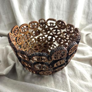 May include: A decorative bowl constructed from numerous dark brown, textured walnut shell halves joined together to form a rounded, open-work lattice structure. The interior and exterior surfaces reveal the intricate, hollowed-out patterns.