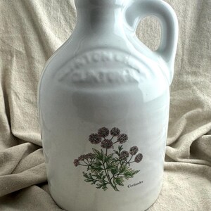 May include: White ceramic jug with a handle and a floral illustration of coriander. The jug has a glossy finish and a rounded shape, with the word "Coriander" printed below the illustration.